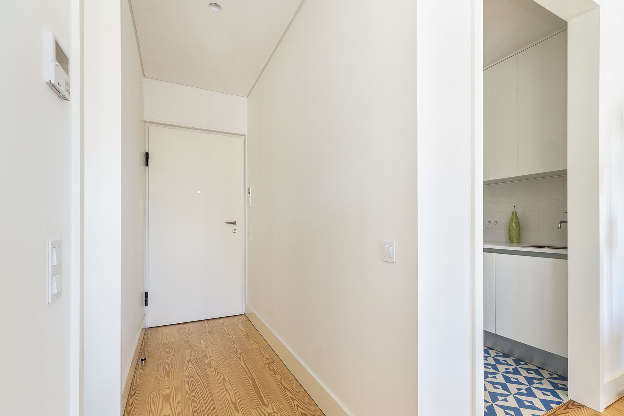 A hallway with a wooden floor leading to a white door.