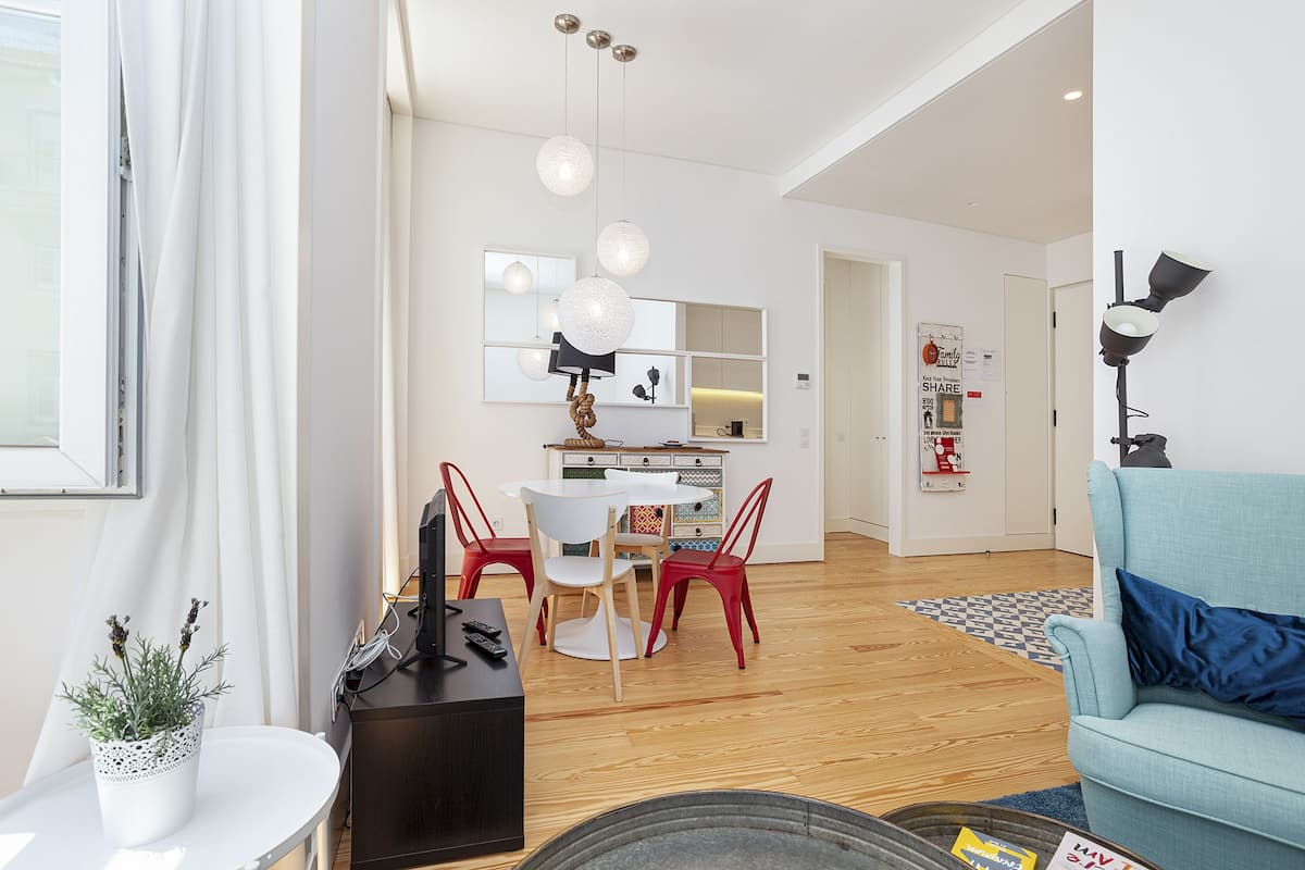 A modern living room with a sofa, a dining area with a table and chairs, and a kitchen in the background.