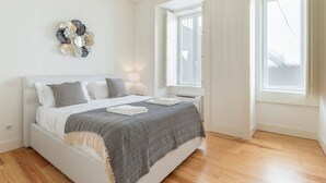 A modern bedroom with a bed, bedside lamps, a decorative wall piece, and a window with curtains. - Gonzalo's Guest Apartments - Luxury Baixa (Lisbon)