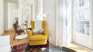 A bright living room with a yellow armchair, a round coffee table, and a view of a building through large windows. - Gonzalo's Guest Apartments - Luxury Baixa (Lisbon)
