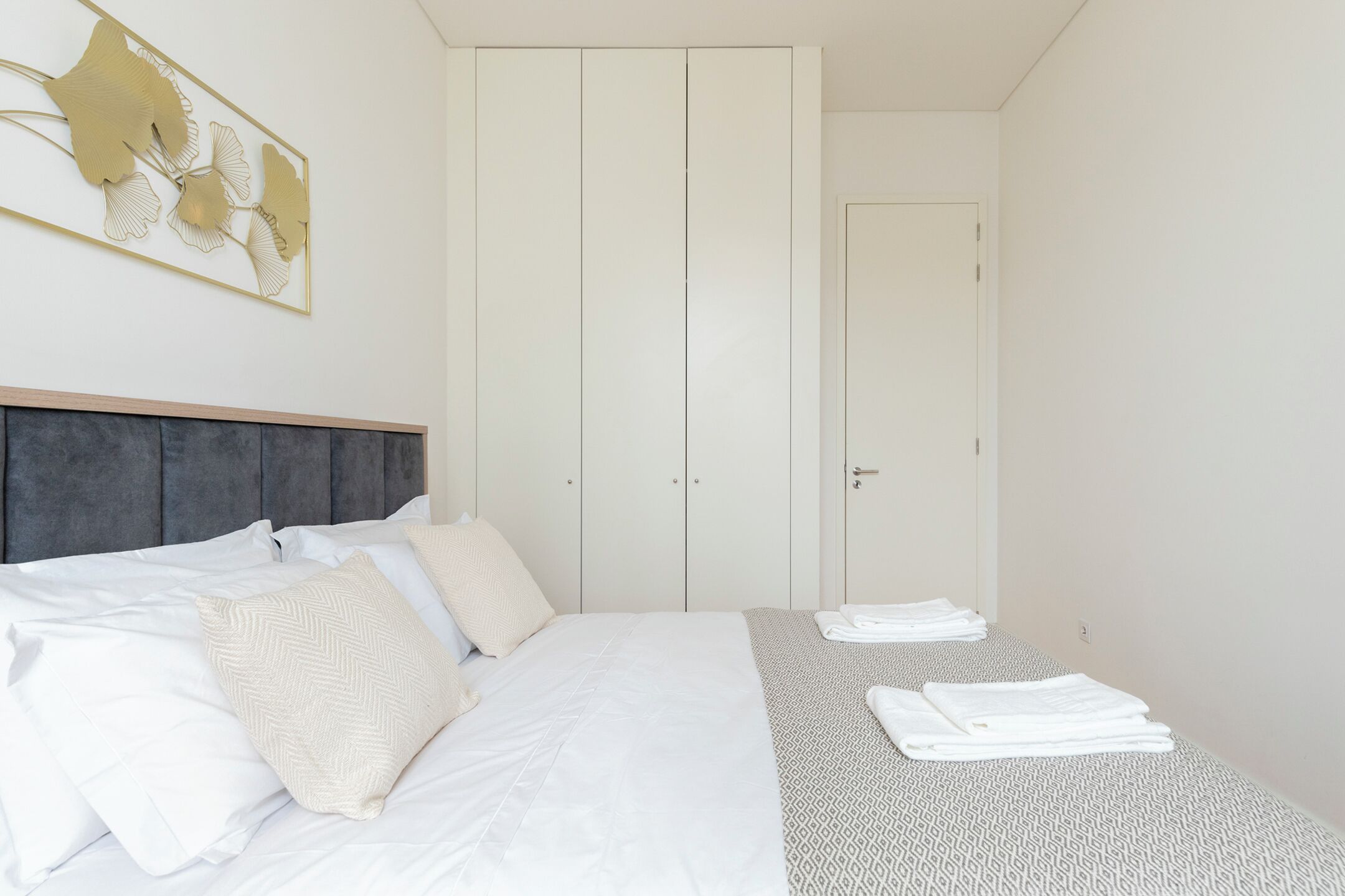 A bedroom with a bed, a headboard, a wardrobe, and a wall-mounted artwork.