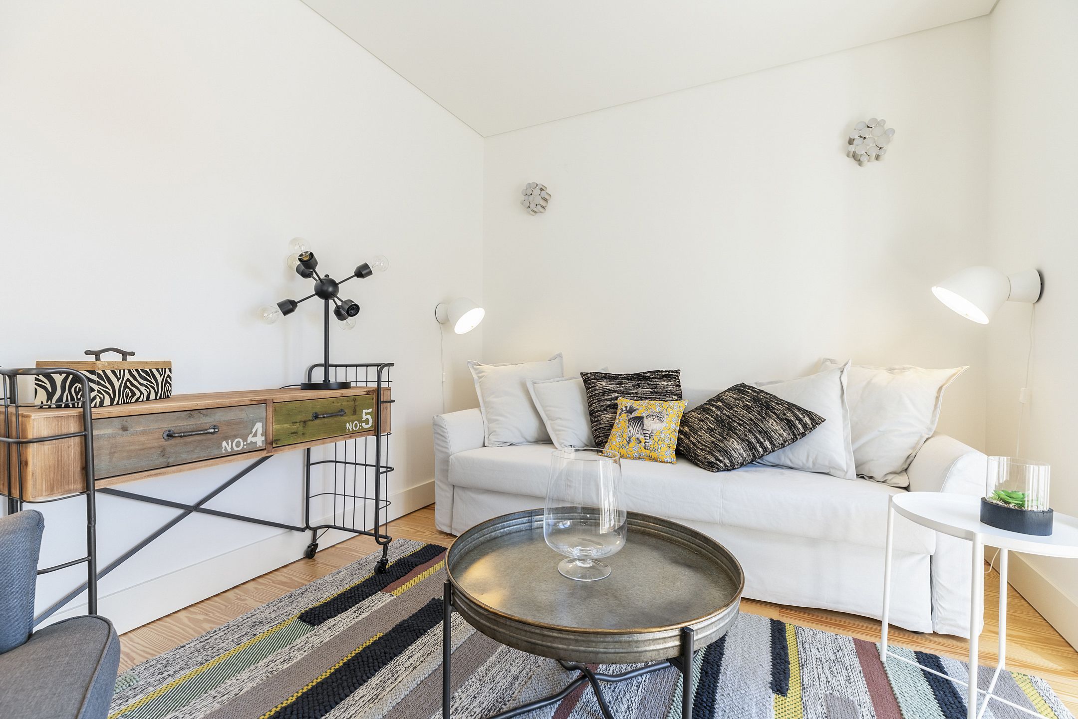 A modern living room with a white sofa, a coffee table, a wooden side table, and a patterned rug.