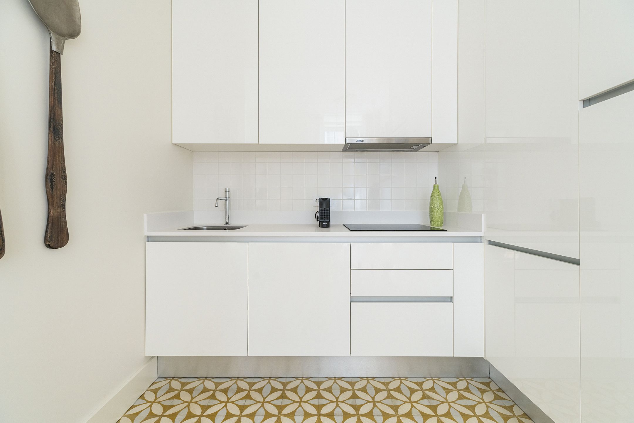A modern kitchen with white cabinets, a stainless steel sink, and a patterned tile floor.