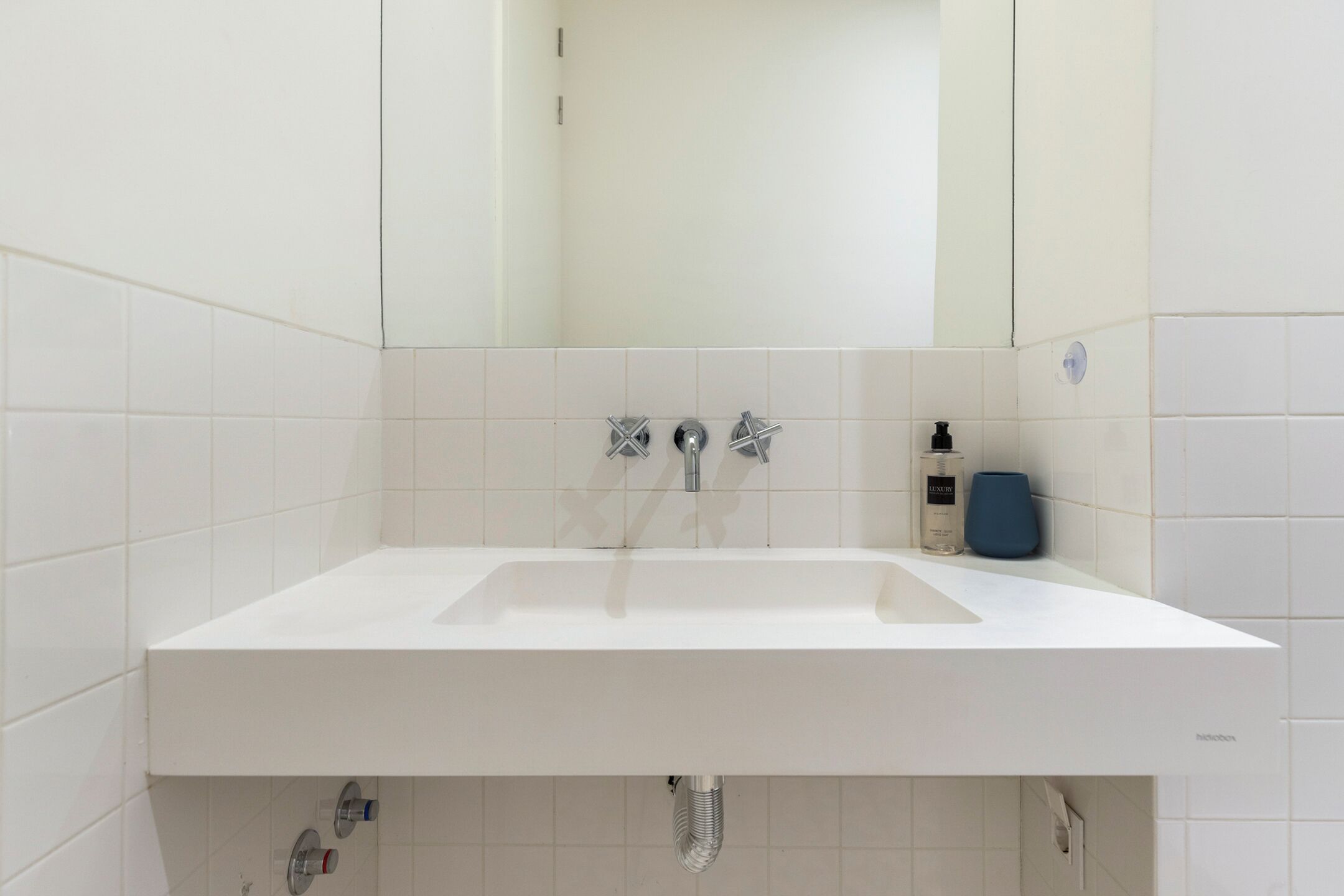 A modern bathroom with a white sink, two faucets, and a mirror above.