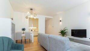 A modern living room with a grey sofa, teal armchair, and a flat-screen TV mounted on the wall. - Gonzalo's Guest Apartments - Luxury Baixa (Lisbon)