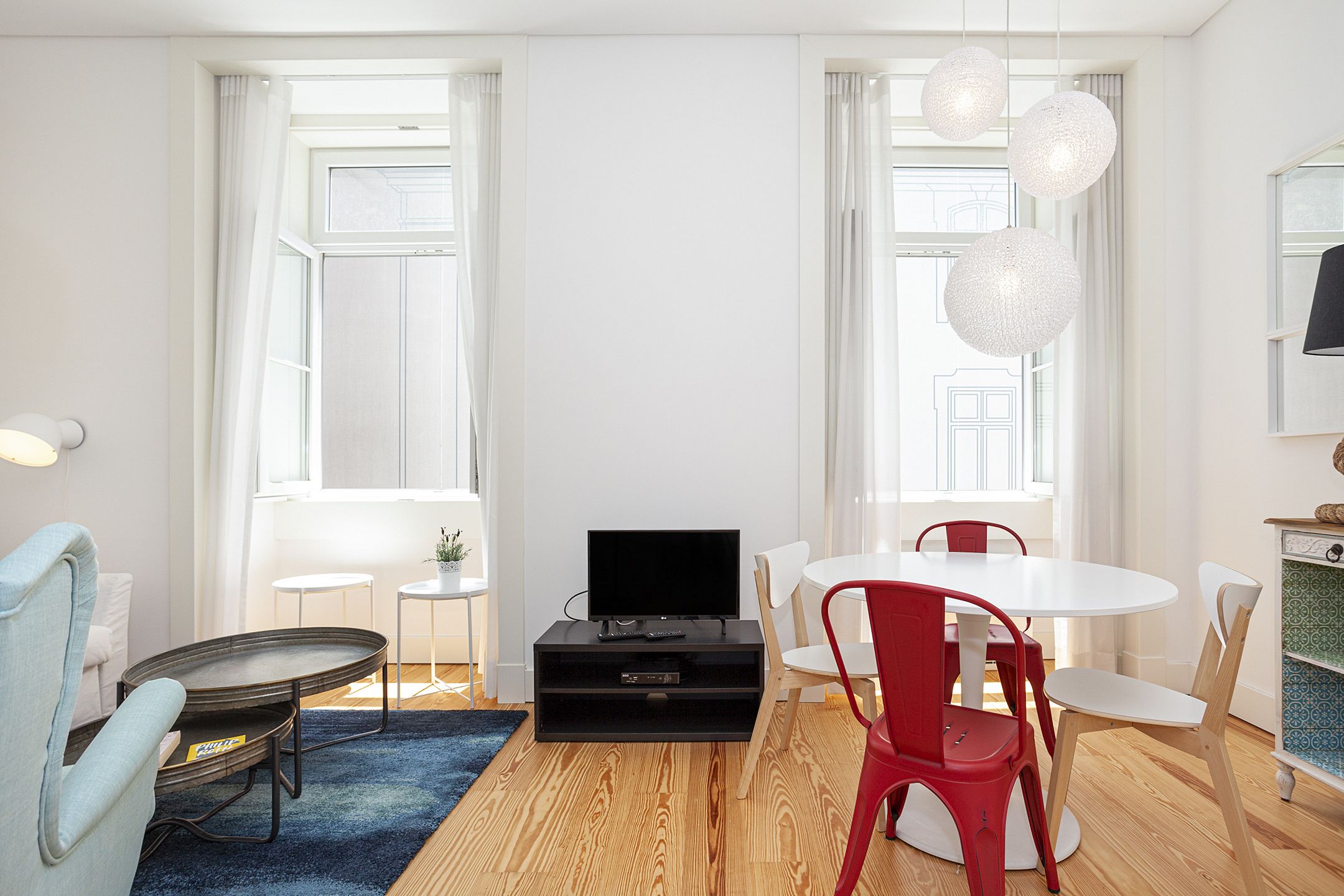 A modern living room with a flat-screen TV, a dining table with chairs, a sofa, and a small side table.