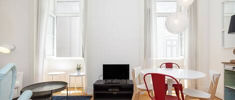 A modern living room with a flat-screen TV, a dining table with chairs, a sofa, and a small side table.