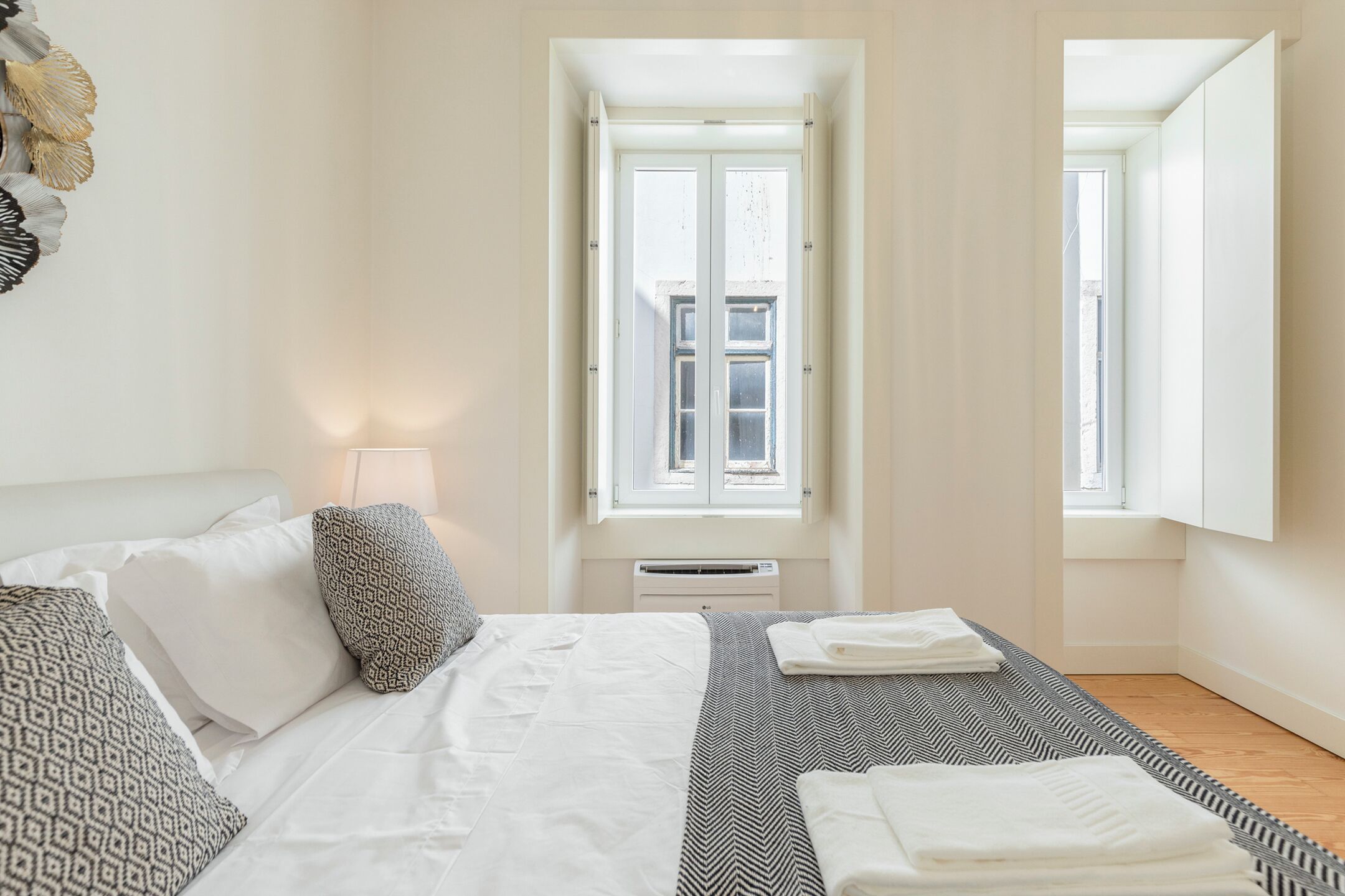 A bedroom with a bed, pillows, a bedside table with a lamp, and a window with a view of the outside.