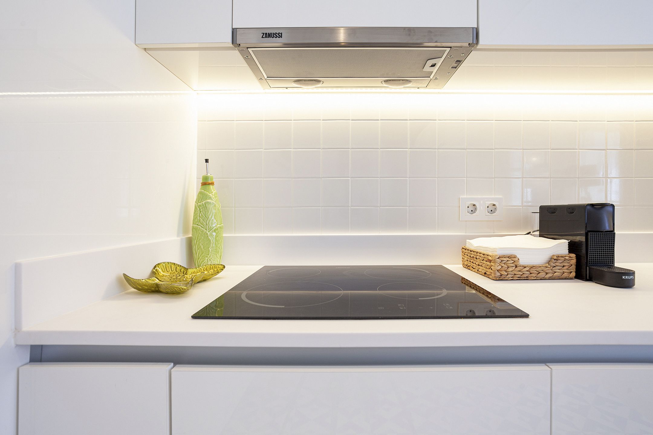 A modern kitchen with a built-in stove, a kettle, and a small island with a cutting board.