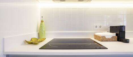 A modern kitchen with a built-in stove, a kettle, and a small island with a cutting board.