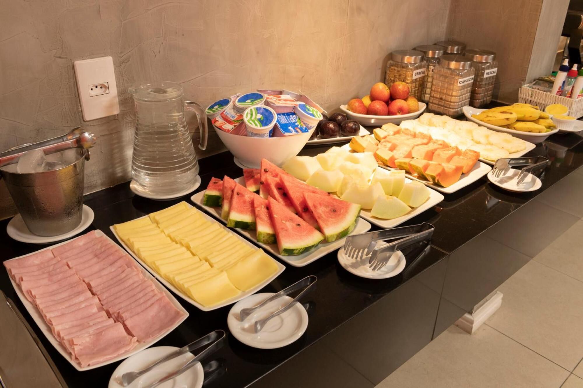A buffet with various food items including sliced meats, fruits, and dairy products.