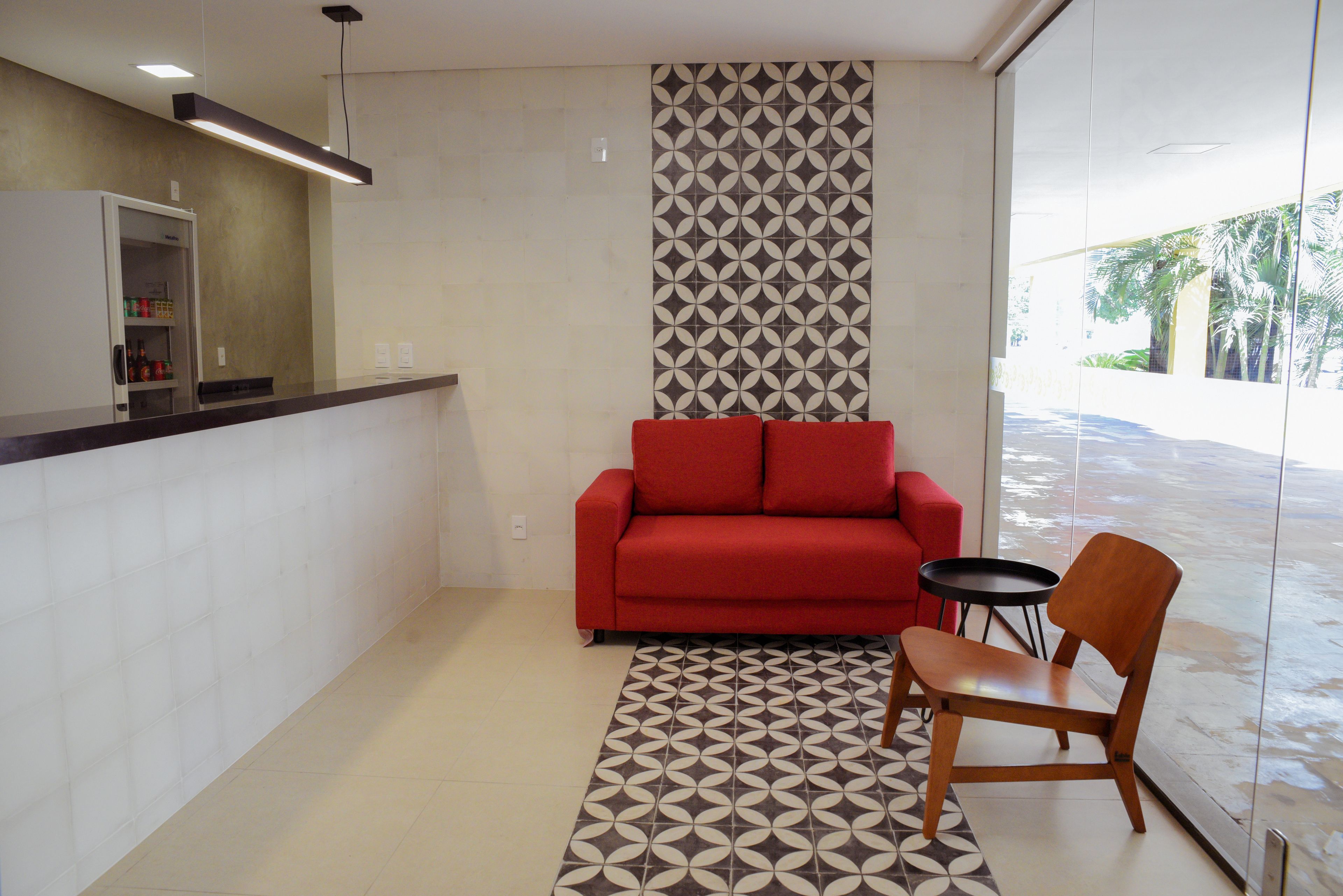 A modern kitchen with a built-in refrigerator, a red sofa, a wooden chair, and a patterned rug.
