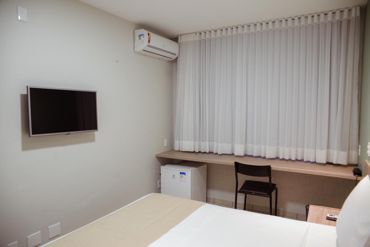 Una habitación de hotel con cama, escritorio con silla, televisión y aire acondicionado.