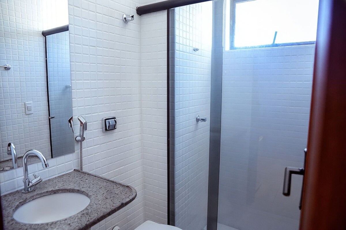A bathroom with a granite countertop sink, a mirror, and a glass-enclosed shower.