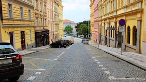 Mukulakivikatu, jonka varrella on rivissä keltaisia rakennuksia, parkkeerattuja autoja ja liikennemerkki, joka kieltää pysäköinnin.