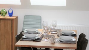 Una mesa de comedor dispuesta con platos, vasos y cubiertos, con una vista a una ventana y un radiador al fondo.