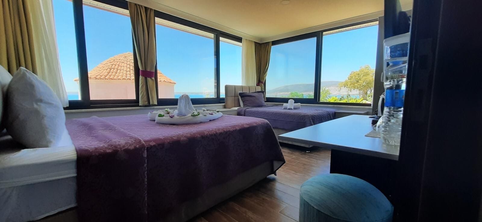 A hotel room with two beds, a small table, and a view of the sea.