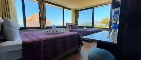 A hotel room with two beds, a small table, and a view of the sea.