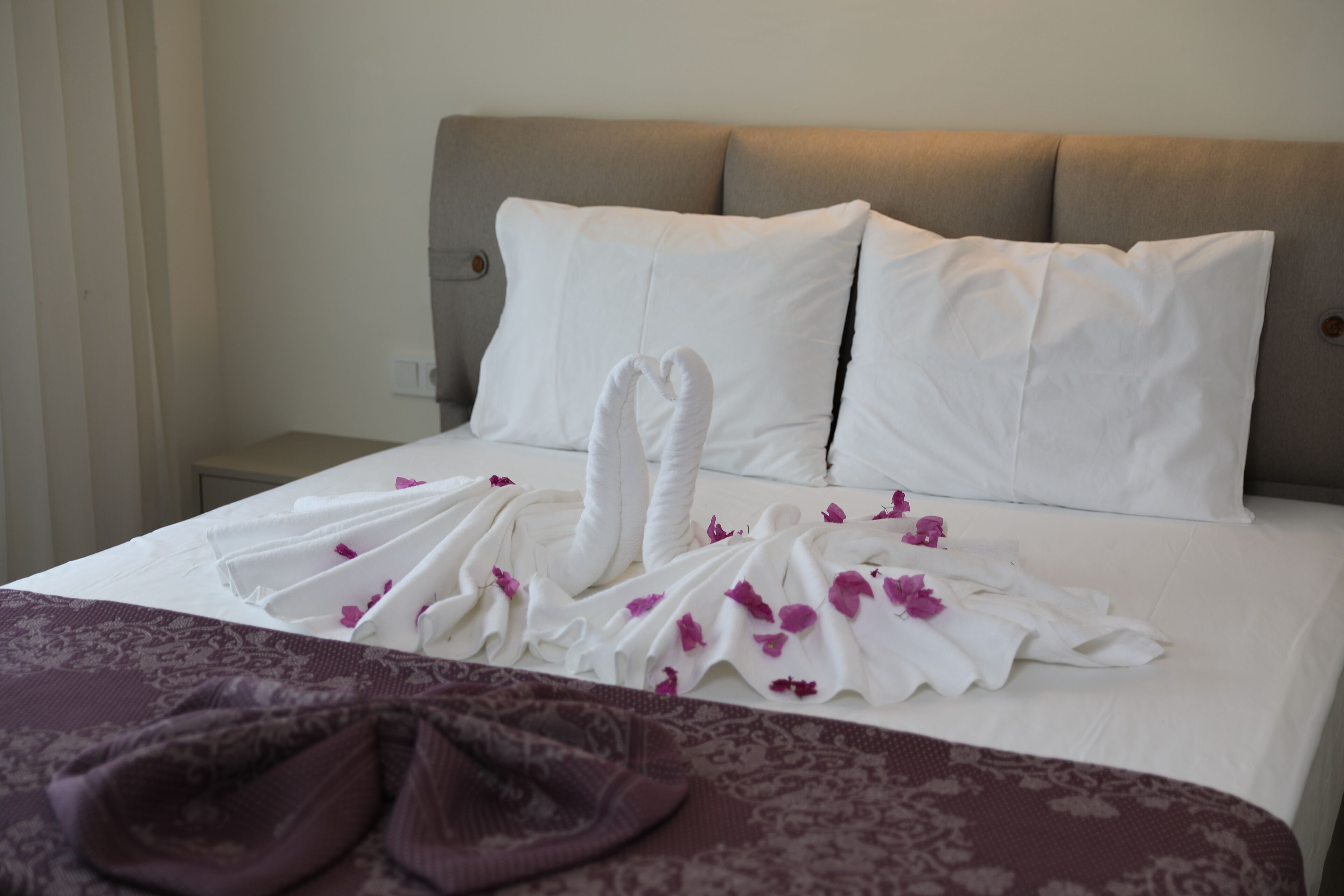 A neatly made bed with white linens and a heart-shaped towel arrangement.