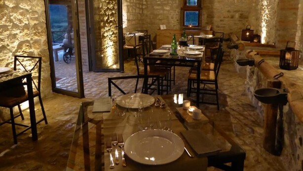 A rustic dining area with stone walls, wooden beams, and a stone floor. Tables are set with plates, glasses, and cutlery. - Pietre di Fiume (San Giorgio del Sannio)