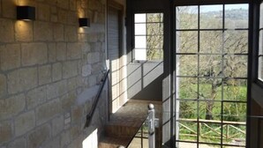 A staircase with stone walls and wooden beams, leading to a large window with a view of trees. - Pietre di Fiume (San Giorgio del Sannio)