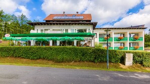 A two-story building with a cafe on the ground floor, solar panels on the roof, and a green hedge in front. - Hotel & Café PANORAMA (Braunlage)