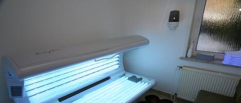 Una cama bronceadora en una habitación con un radiador, una mesita pequeña y una alfombra estampada.