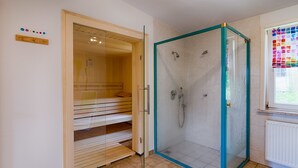 A sauna room with a glass door, a wooden bench, and a window with a colorful view. - Hotel & Café PANORAMA (Braunlage)