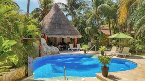 A pool with lounge chairs, a thatched-roof structure, and tropical vegetation. - Villa #1 -Isla Retreats: Tropical Gardens and Pool (Isla Mujeres)