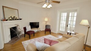 Una sala de estar con chimenea, ventilador de techo, televisor y un ventanal grande.