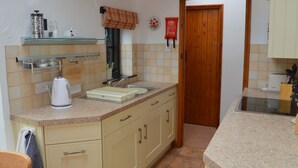 A kitchen with a granite countertop, a coffee maker, a sink, and wooden cabinets. - Shipload Cottage (Bideford)