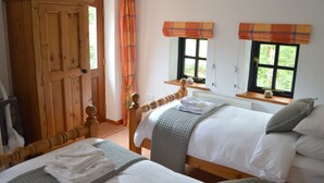 A bedroom with two beds, a wooden wardrobe, a window with curtains, and a radiator. - Shipload Cottage (Bideford)