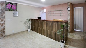 Un área de recepción con un mostrador de madera, un reloj en la pared y plantas en macetas.