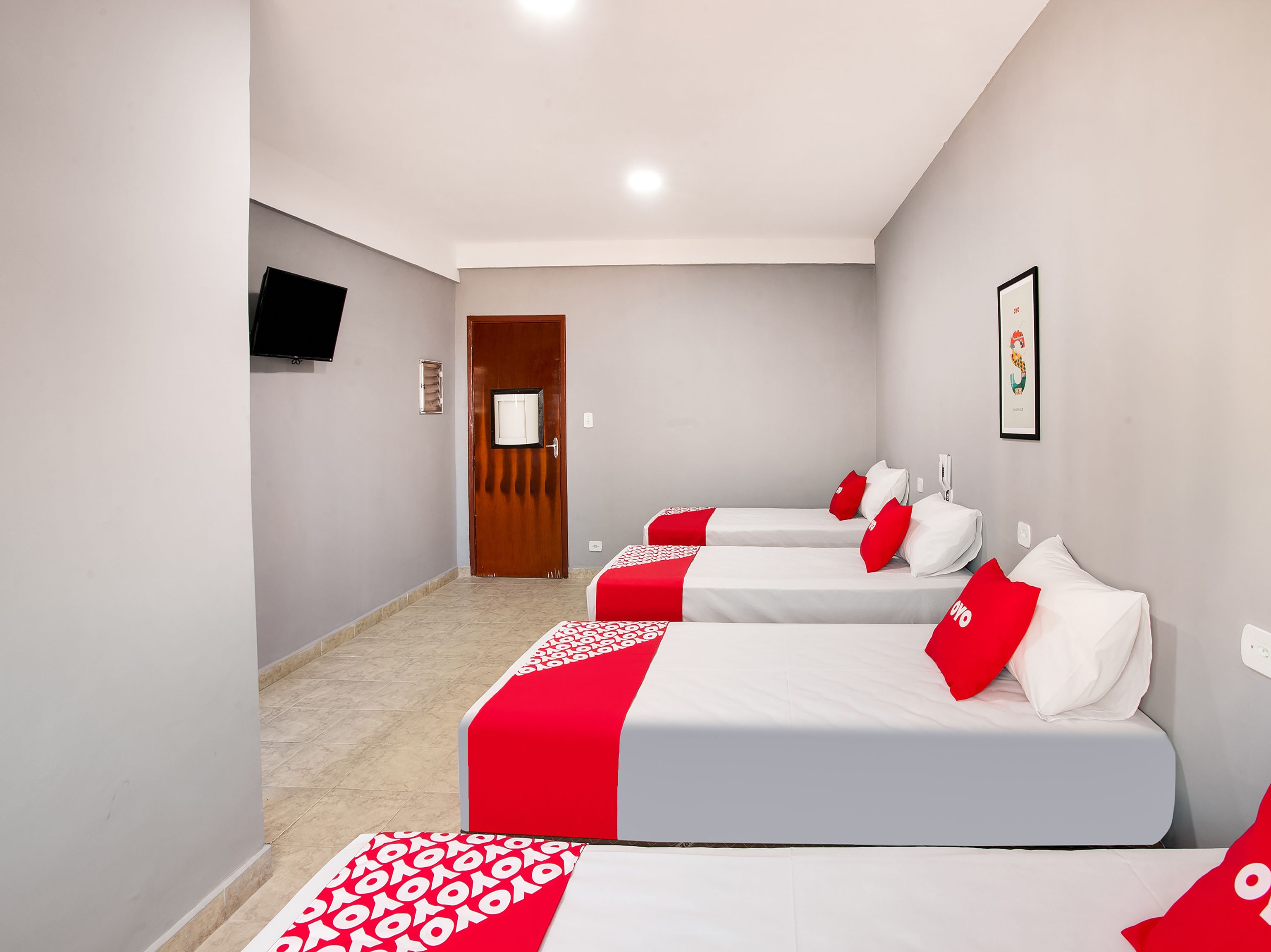 Habitación de hotel con tres camas, un televisor en la pared y una puerta.