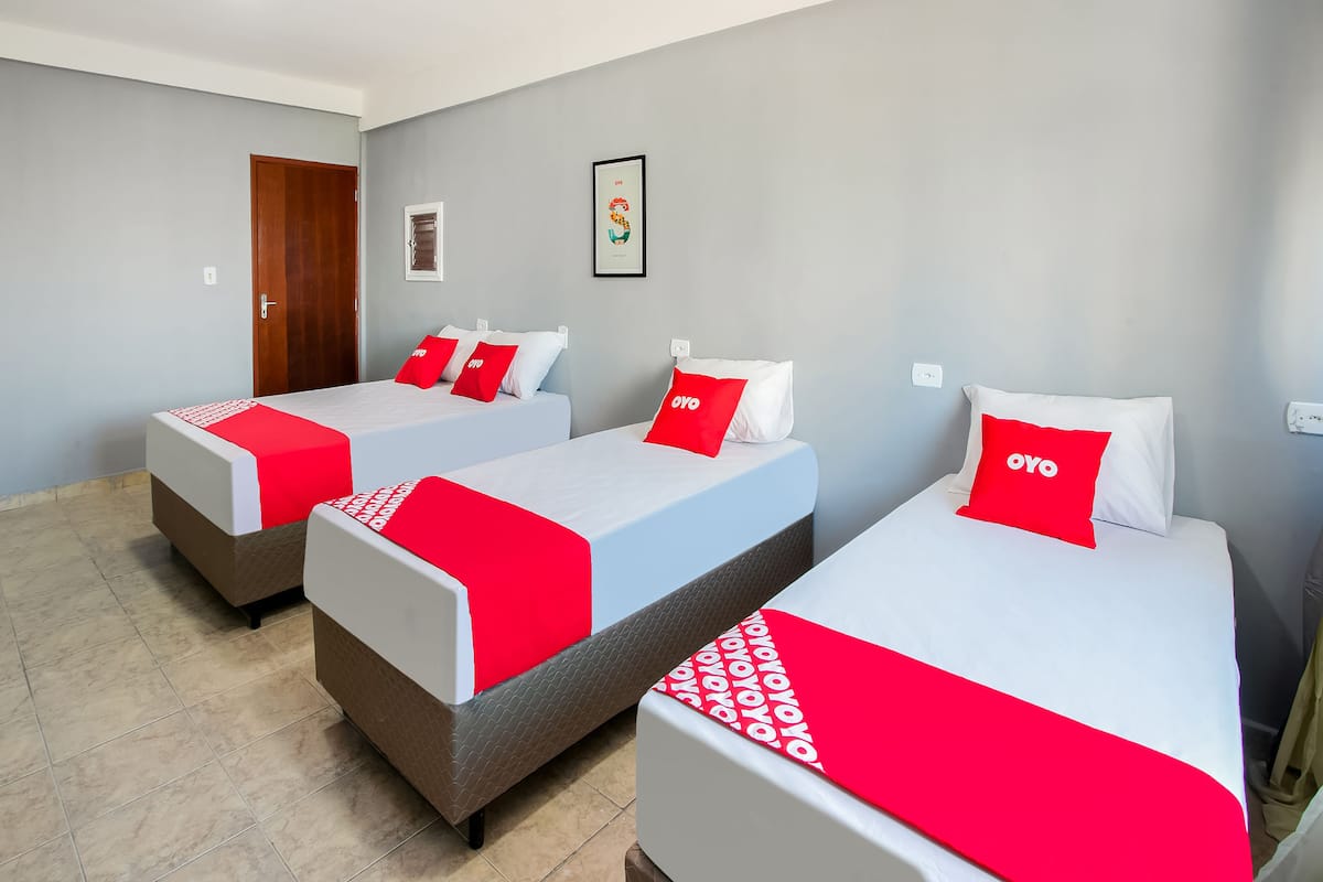 Una camera d'albergo con tre letti, ognuno con copripiumini e cuscini rossi e bianchi.