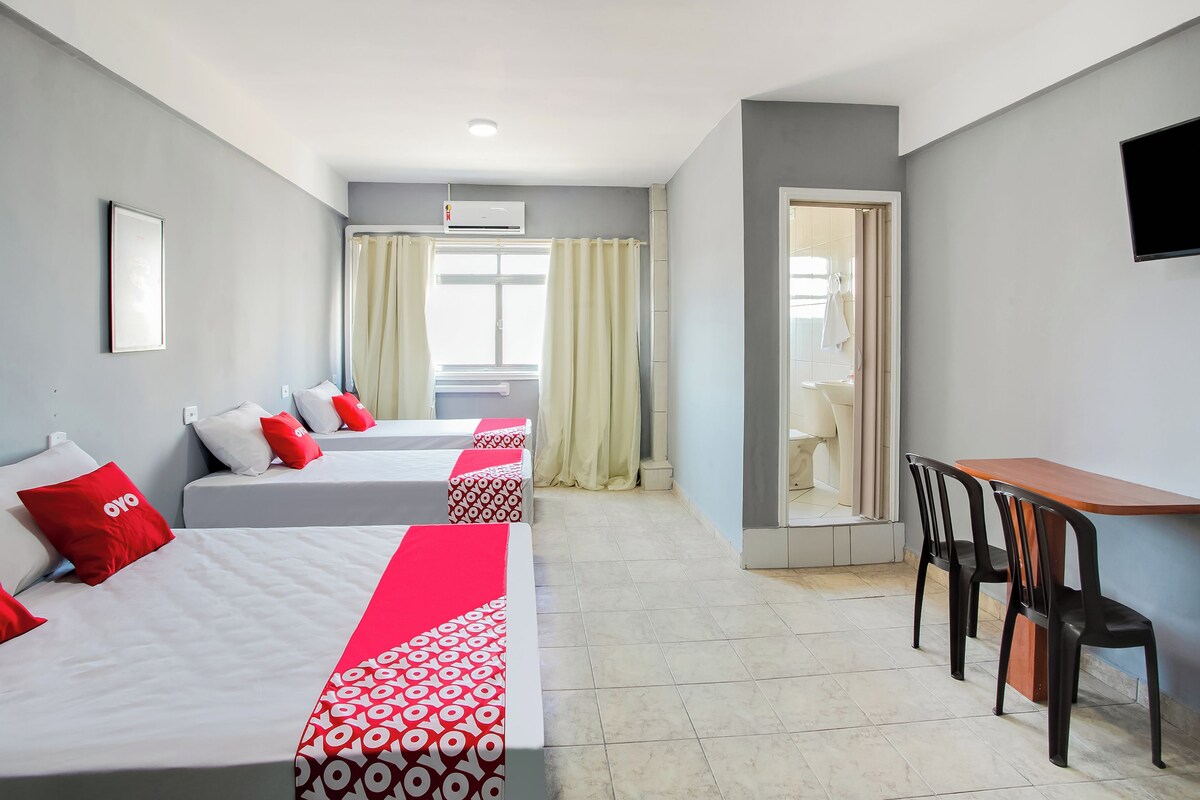 Une chambre d’hôtel avec deux lits, un bureau, des chaises, une télévision et une salle de bain visible à travers une porte ouverte.