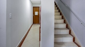 Un pasillo estrecho con una puerta de madera al final, que da a una escalera con escalones beige y marrones.