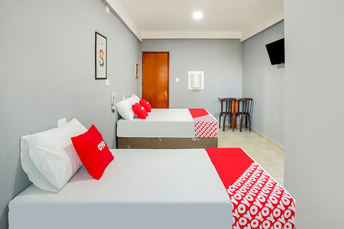 Una camera d'albergo con due letti, una porta in legno, un tavolino con sedie e una TV a parete.