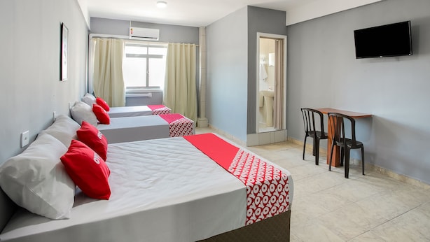 Habitación de hotel con dos camas, televisión, escritorio y baño visible a través de una puerta abierta.
