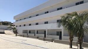 A modern multi-story building with a flat roof, multiple balconies, and a paved courtyard.