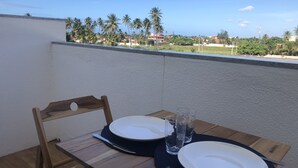 A wooden table with two white plates, two glasses, and a fork on a balcony with a view of palm trees and buildings.