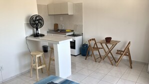 A compact kitchen with a gas stove, a sink, and a fan. There is a small dining table with chairs and a bed with a blue bedspread.