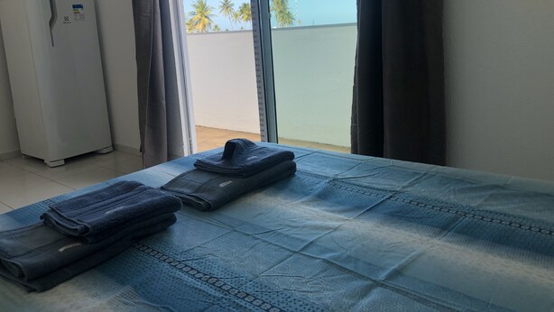 A hotel room with a bed, a folded towel, and a refrigerator.