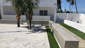 A paved outdoor area with a herringbone pattern, a section of artificial green grass, and a concrete planter.
