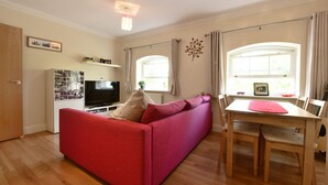 A living room with a red sofa, a TV, a dining table with chairs, and a window with curtains.