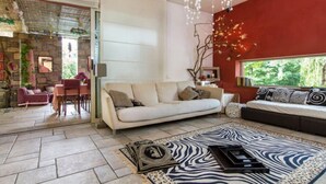 A modern living room with a white sofa, a black sofa with patterned cushions, a zebra-patterned rug, and a stone fireplace. - B&B La Colombera (Lessona)