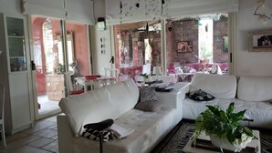 A living room with a white sofa, a coffee table with a plant, and a patterned rug. There is a glass door leading to an outdoor area with a brick wall and a table with chairs. - B&B La Colombera (Lessona)