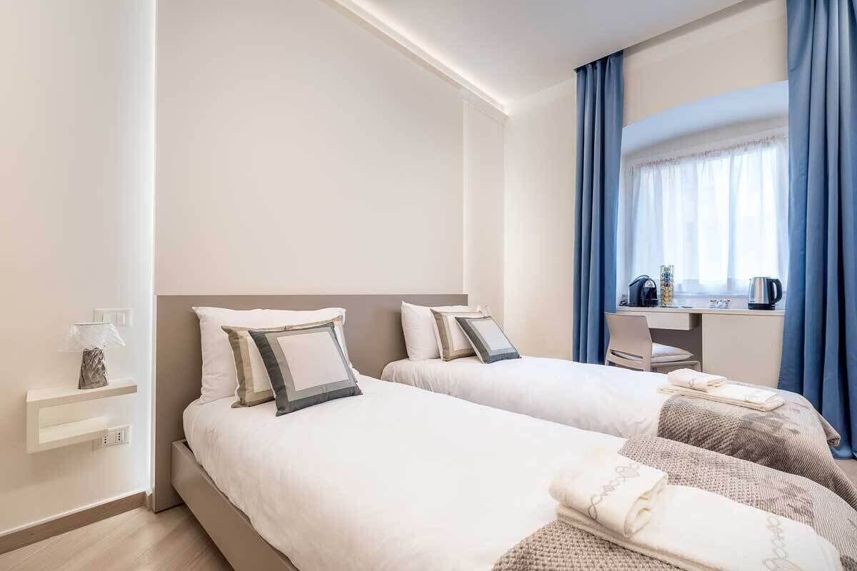 Une chambre d’hôtel avec deux lits, un bureau et une fenêtre avec des rideaux.