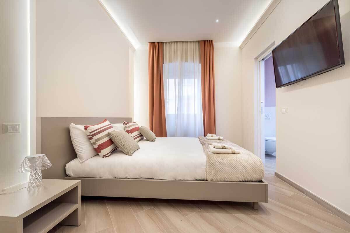 Une chambre à coucher moderne avec un lit, un téléviseur fixé au mur et une fenêtre avec des rideaux.