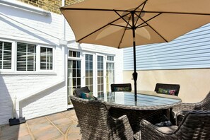 A patio with wicker furniture, a glass table, and a beige umbrella. - Grosvenor House (Margate)